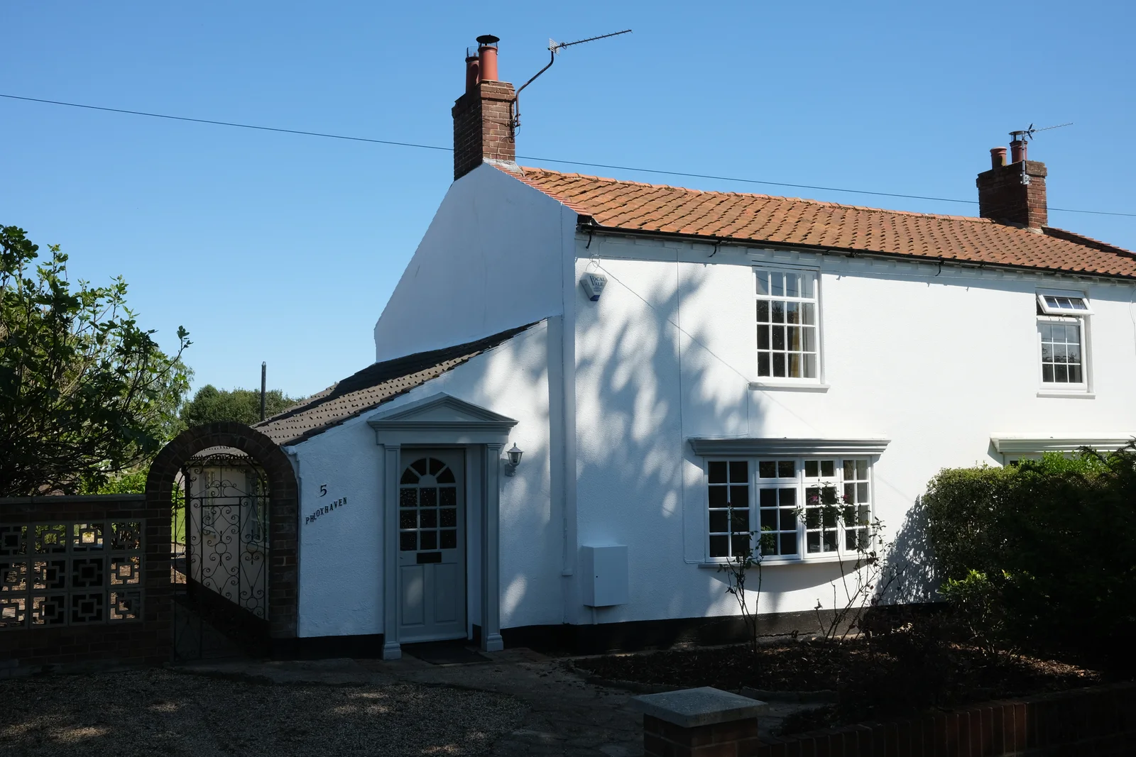 Phloxhaven in Reedham, a white cottage with a tiled roof, grey front door and garden